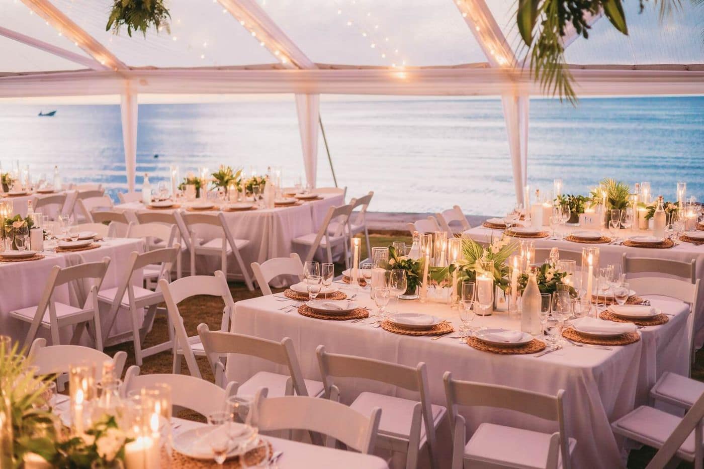 Candlelit reception tables under a clear tent overlooking the sea