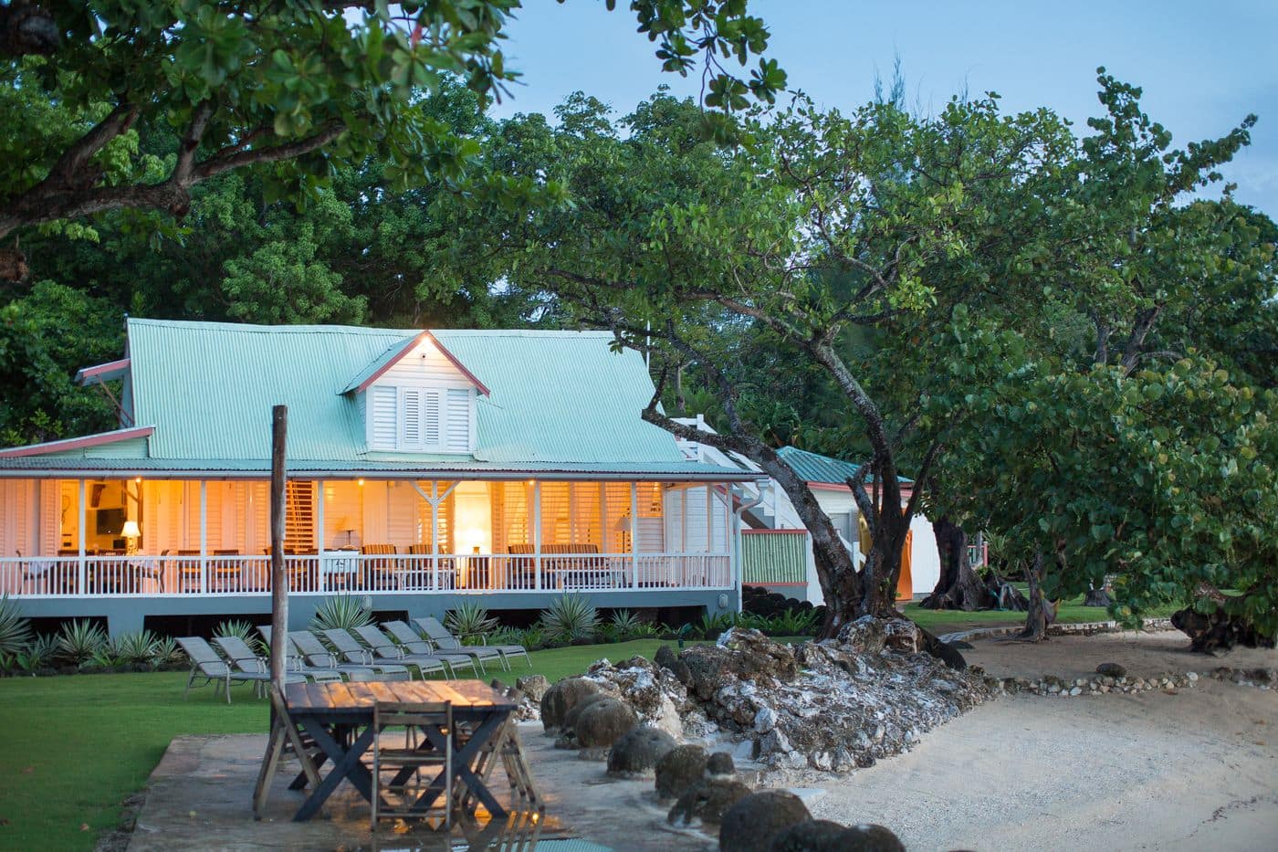 The great house at dusk, lights glowing on the wraparound veranda