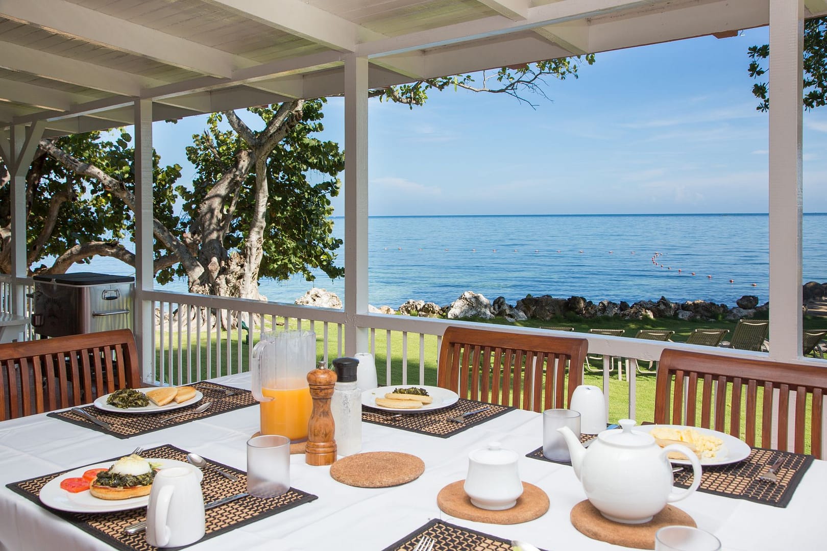 Breakfast laid on the veranda: a teapot, fresh juice and plates set with a view of the sea