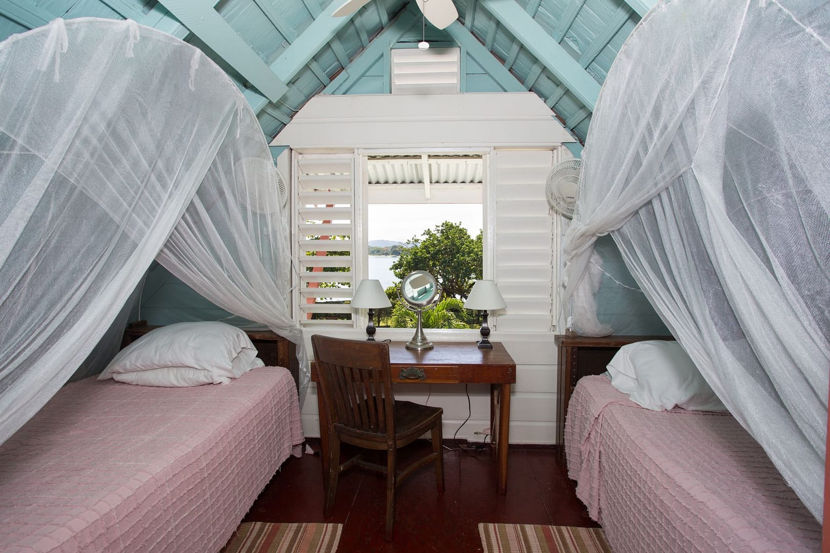Upstairs: twin beds under white nets on either side of a desk and a louvred window