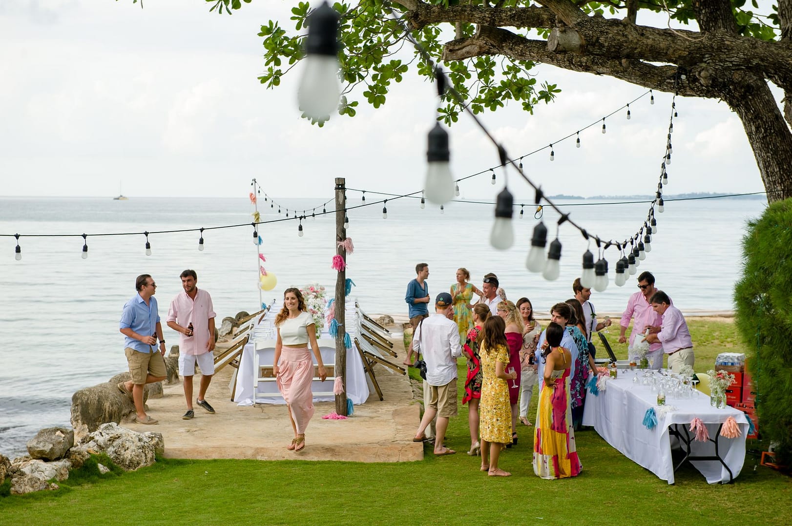 Guests gathered along the seawall under string lights at golden hour