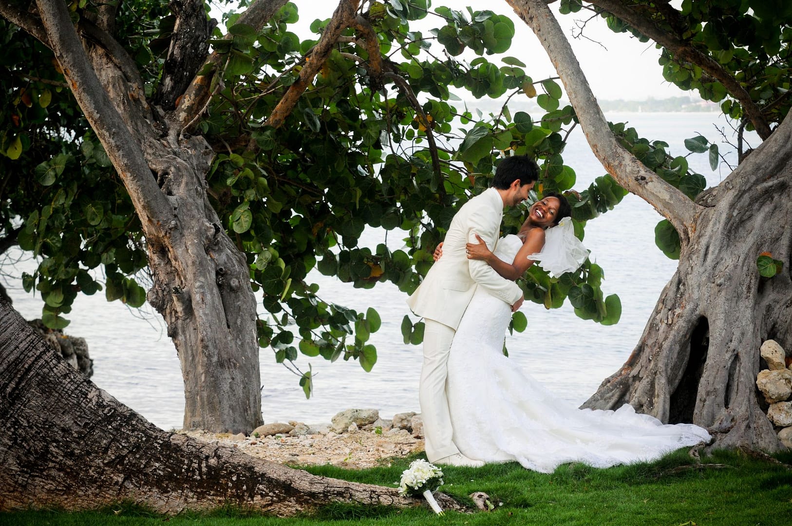 The newlyweds kissing beneath the arching branches of the sea grape trees, the sea behind them