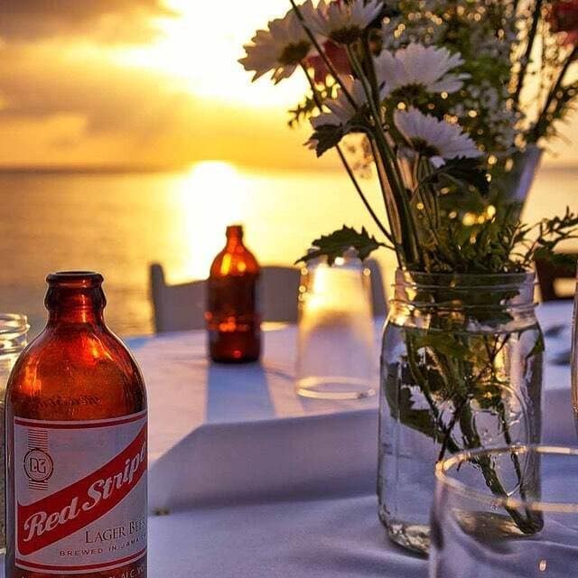 A table set for dinner at sunset, with flowers and a cold Red Stripe